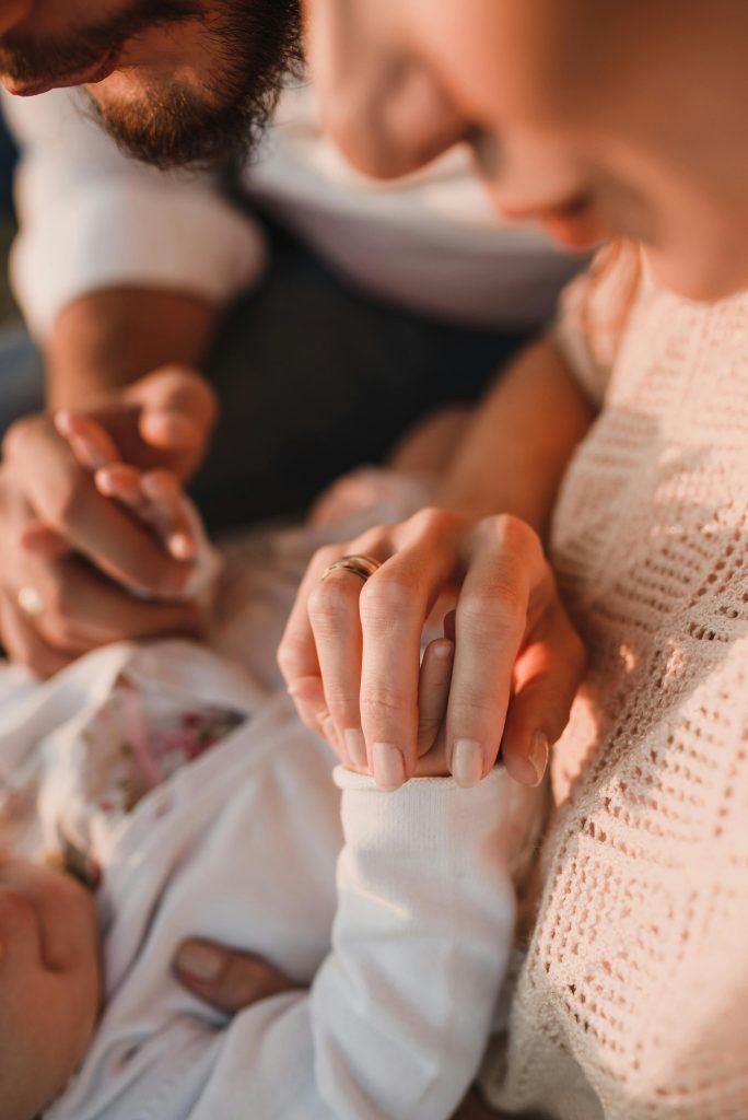 Close-up of parents holding their baby's hand in a warm, intimate setting.