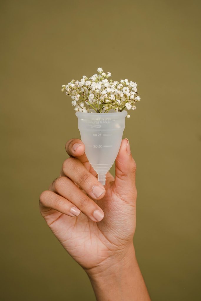 Minimalistic photo of a hand holding a menstrual cup with delicate flowers, symbolizing eco-friendly menstruation.