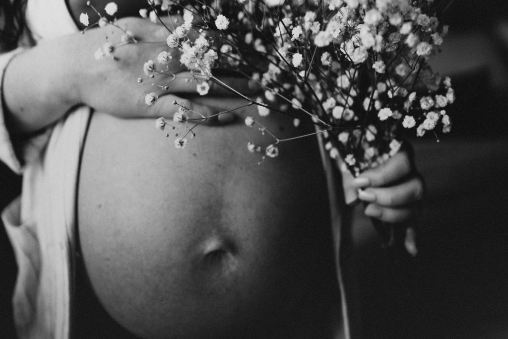 Artistic black and white photo of a pregnant woman holding flowers against her belly.
