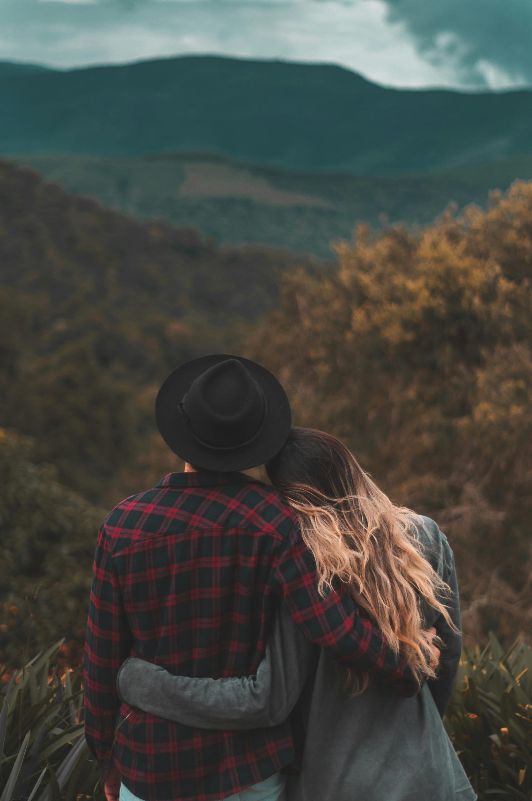 Romantic couple embraces while enjoying a beautiful scenic view of hills during daytime.