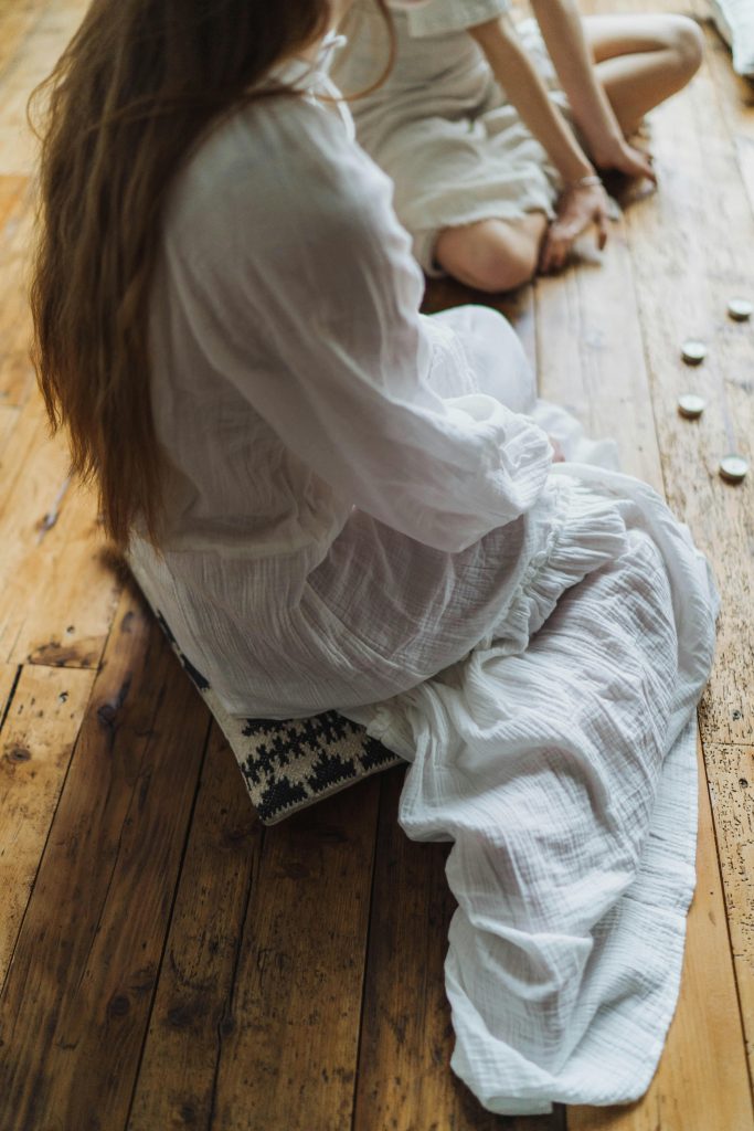 Two women in white sit on wooden floor, engaged in a spiritual ritual.