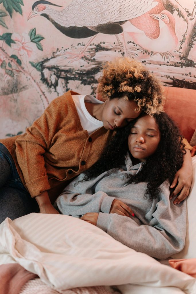 A loving mother embraces her sleeping daughter on a cozy bed, surrounded by warm decor.