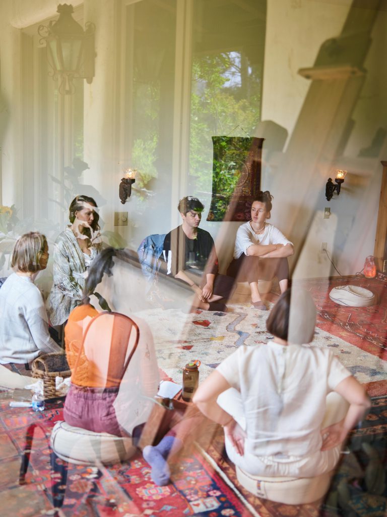 A diverse group sits in a circle during a relaxed meditation session indoors.